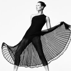 Black and white image of a model moving the sheer dress bottom of a luxury Stuart Weitzman body suit