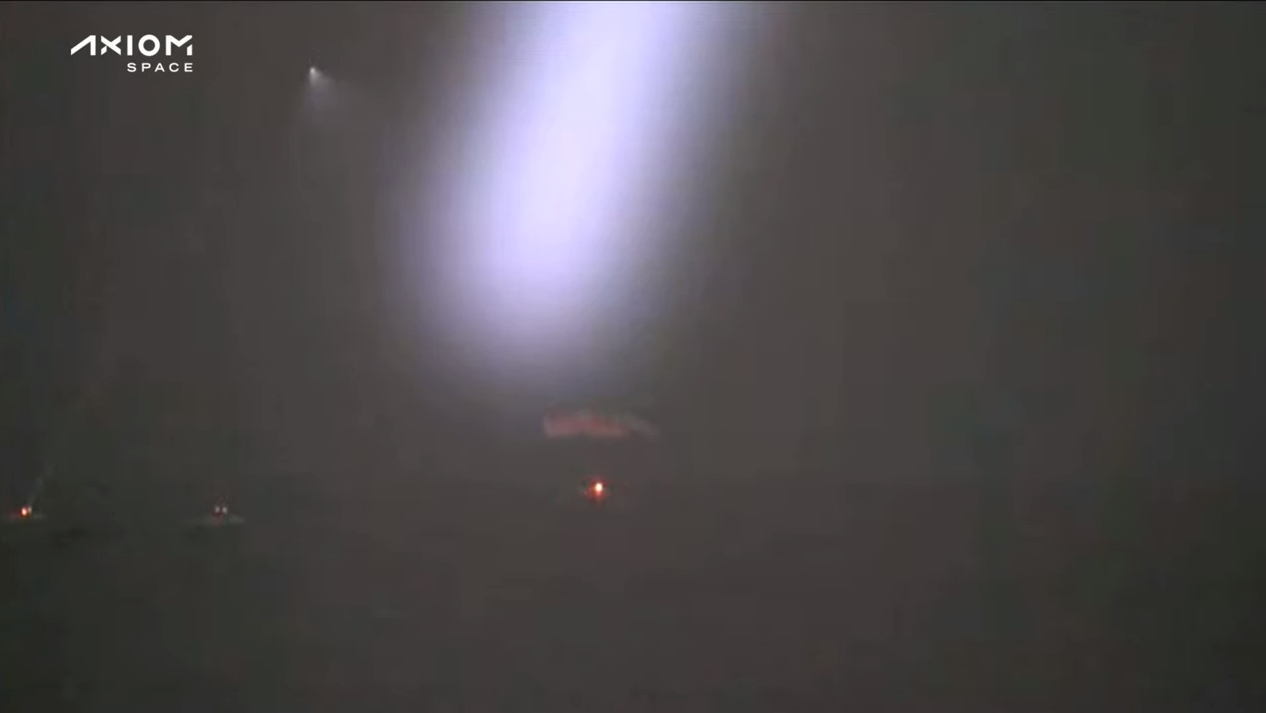 SpaceX Dragon capsule splashing down at night in the Gulf of Mexico with searchlights above.