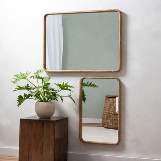 Two rectangle mirrors by a wooden side table with a planter