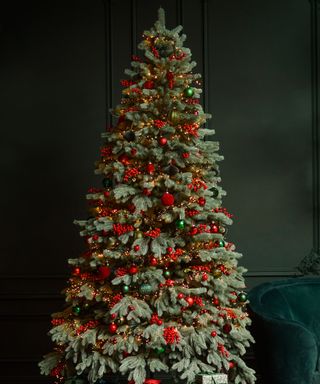 A christmas tree with green and red decorations against a dark green wall with a dark green velvet sofa to the right