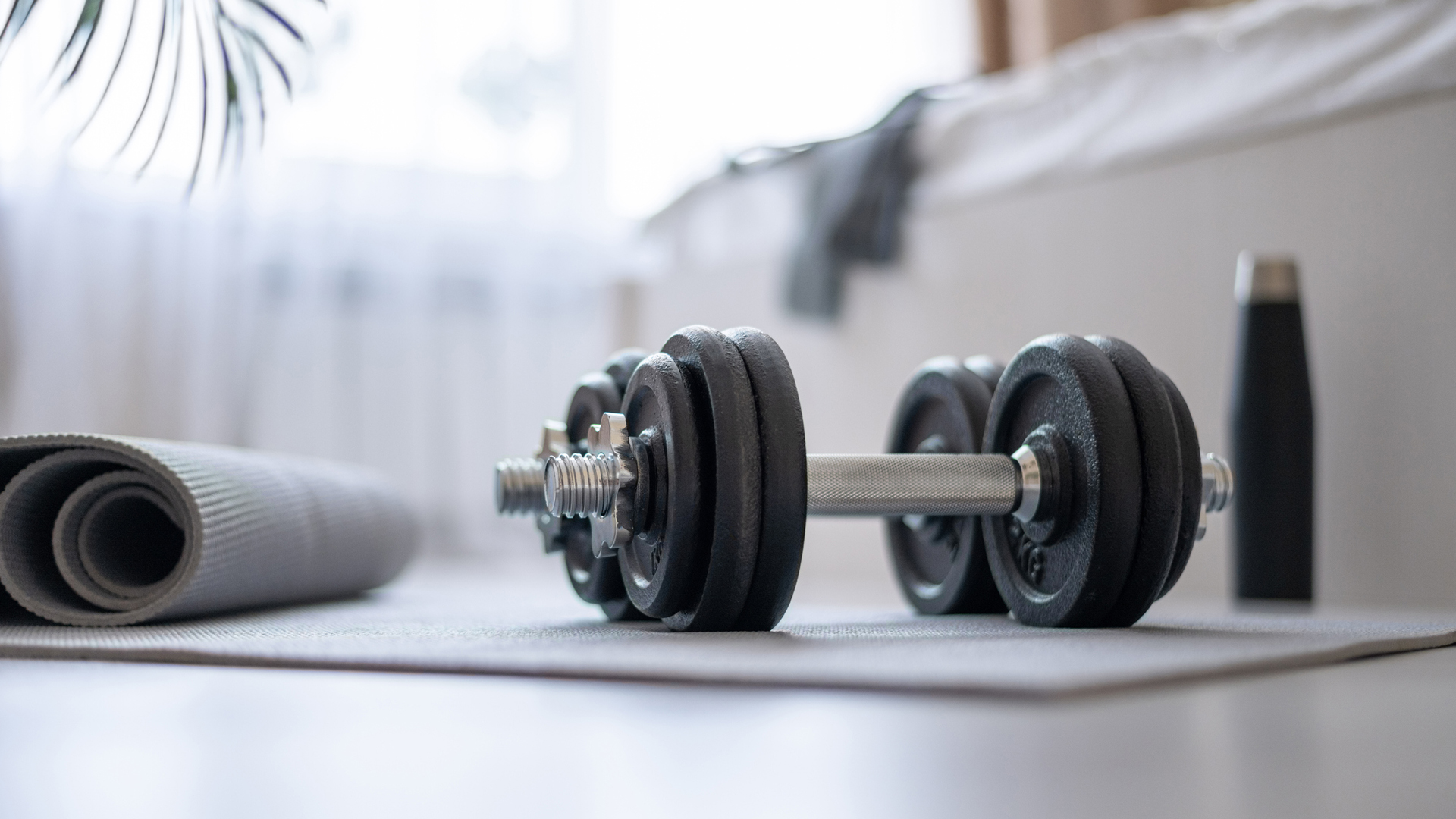 Dumbbells, mats and water on the floor of the bedroom preparing for home sports