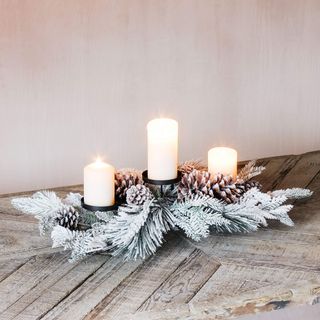 Christmas table centerpiece with frosted white leaves, pine cones and three pillar candles