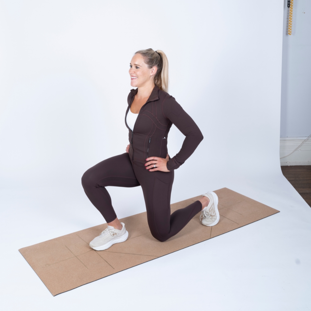 woman wearing black workout clothes performing a lunge on a workout mat against a white background.