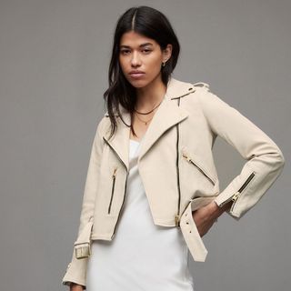 model against a grey background wearing a cream leather jacket from allsaints