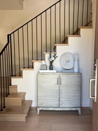 Beige and cream entryway with decorated console table in front of stairs.