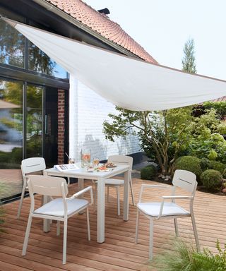 deck with dining table and chairs and a white shade sail overhead