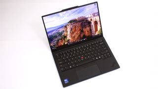 An open, black laptop against a white background with a picture of a building built into a cliffside showing on the screen. 