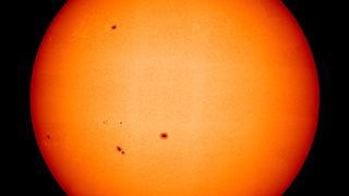 A large image of the sun with a few small dark sunspots