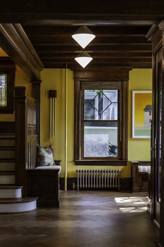 wood panelled entryway with yellow painted walls, herringbone floor, wooden bench, pendant lights