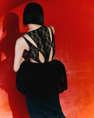 Woman in lace dress facing red wall