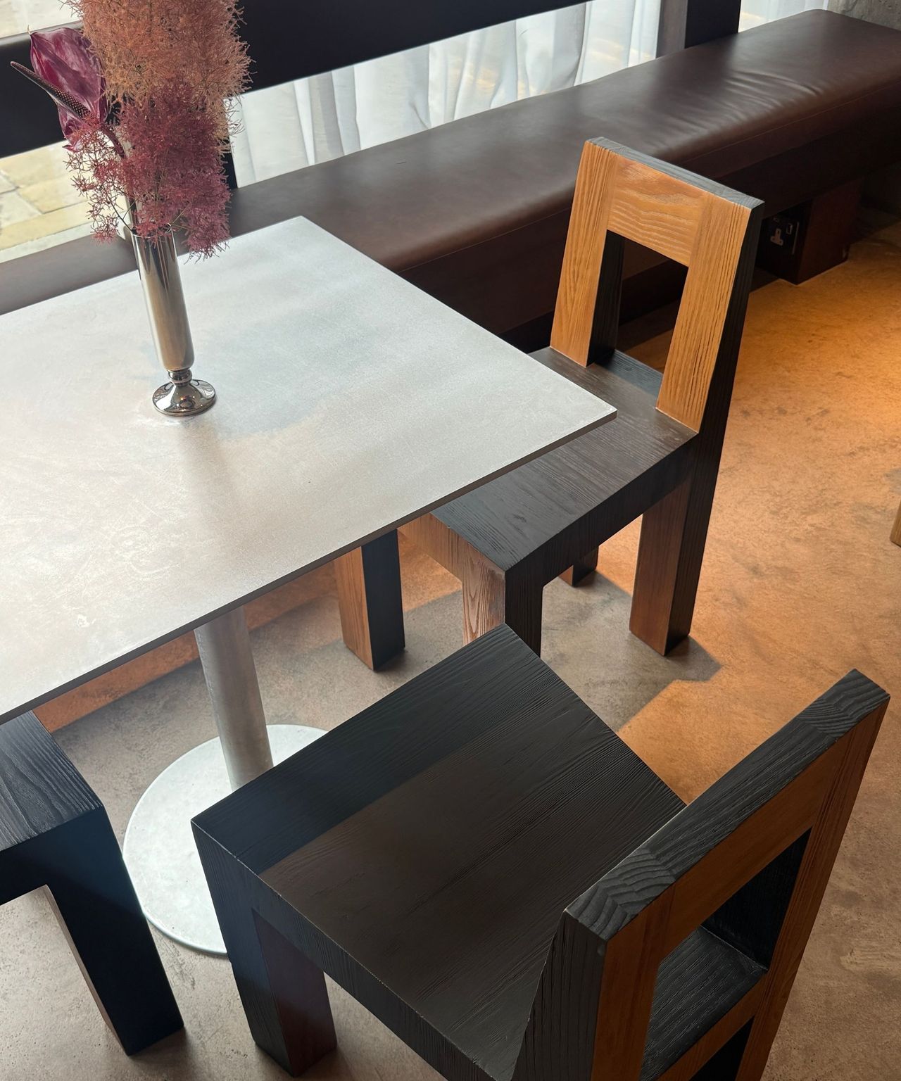 close up of stainless steel table with three timber chairs around it with small silver vase with flowers