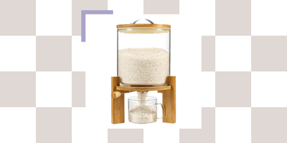 A wood and glass rice dispenser with a measuring cup against a checkerboard grid