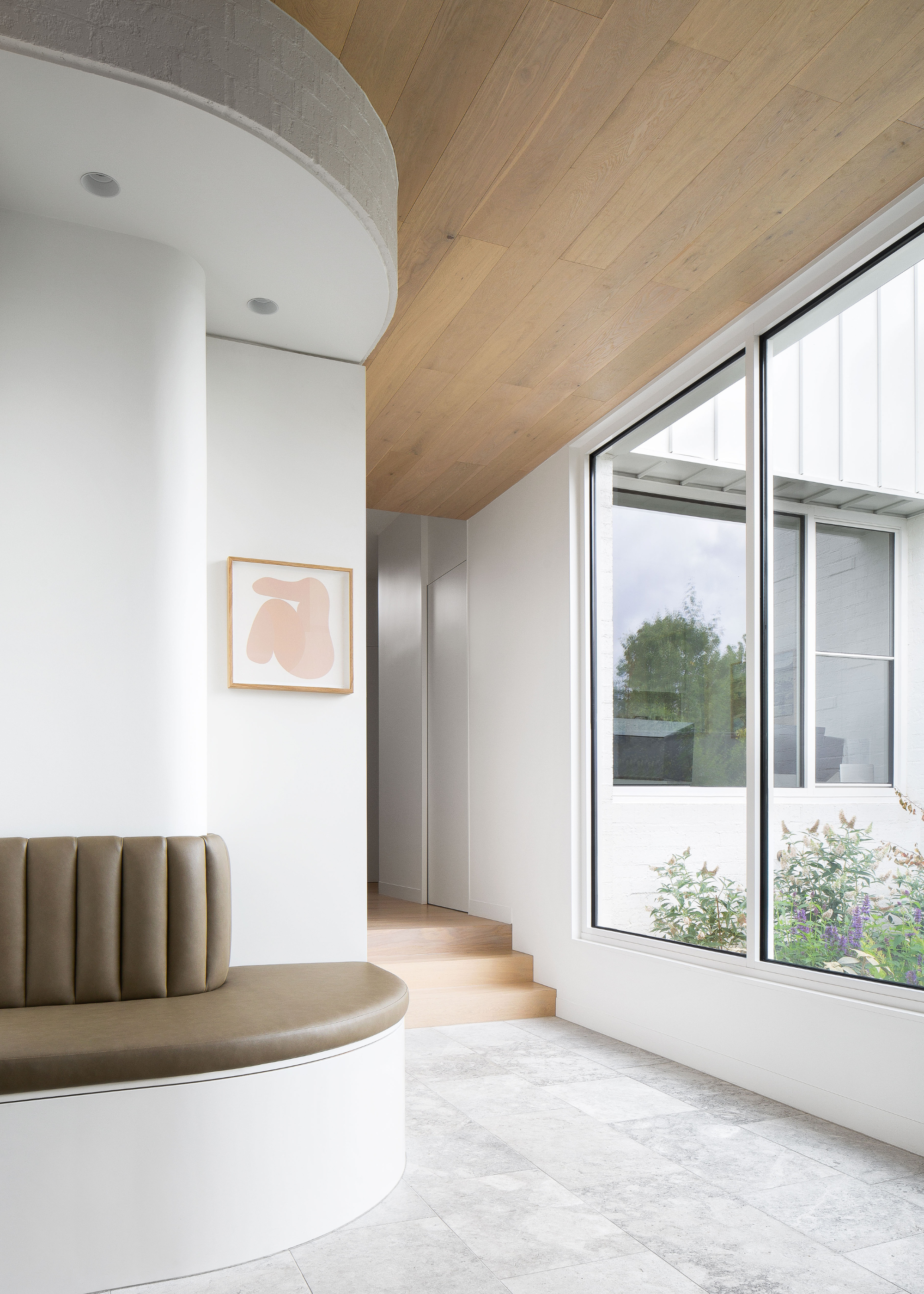 A minimalist living room with large windows, curved olive couch seating and framed art