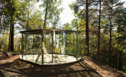 An empty glass and metal pavilion in the forest surrounded by trees. Photographed during the day