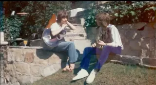 A screengrab from an RCA Victor's Vault video showing George Harrison and Eric Clapton writing "Badge" while in a Los Angeles garden. Harrison is holding a 1913 Gibson Style O acoustic owned by both men