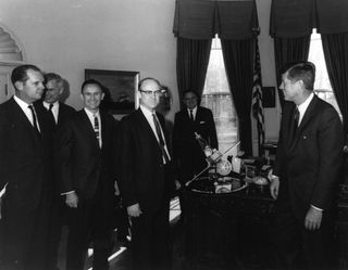 Dr. William H. Pickering, (center) director of NASA's Jet Propulsion Laboratory, presents a model of a Mariner spacecraft to President John F.Kennedy, (right) in 1961. NASA Administrator James Webb is standing directly behind the model.