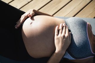 Postpartum exercise: Young pregnant woman doing yoga outdoor - Focus on right hand holding belly