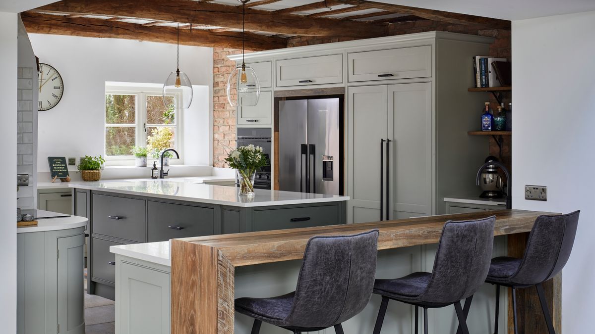 kitchen diner space with exposed beams, soft sage green kitchen cabinets and island with raised seating area made from large wooden block