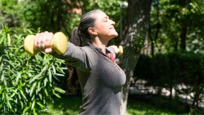 Woman doing lateral raise exercise in garden sunshine
