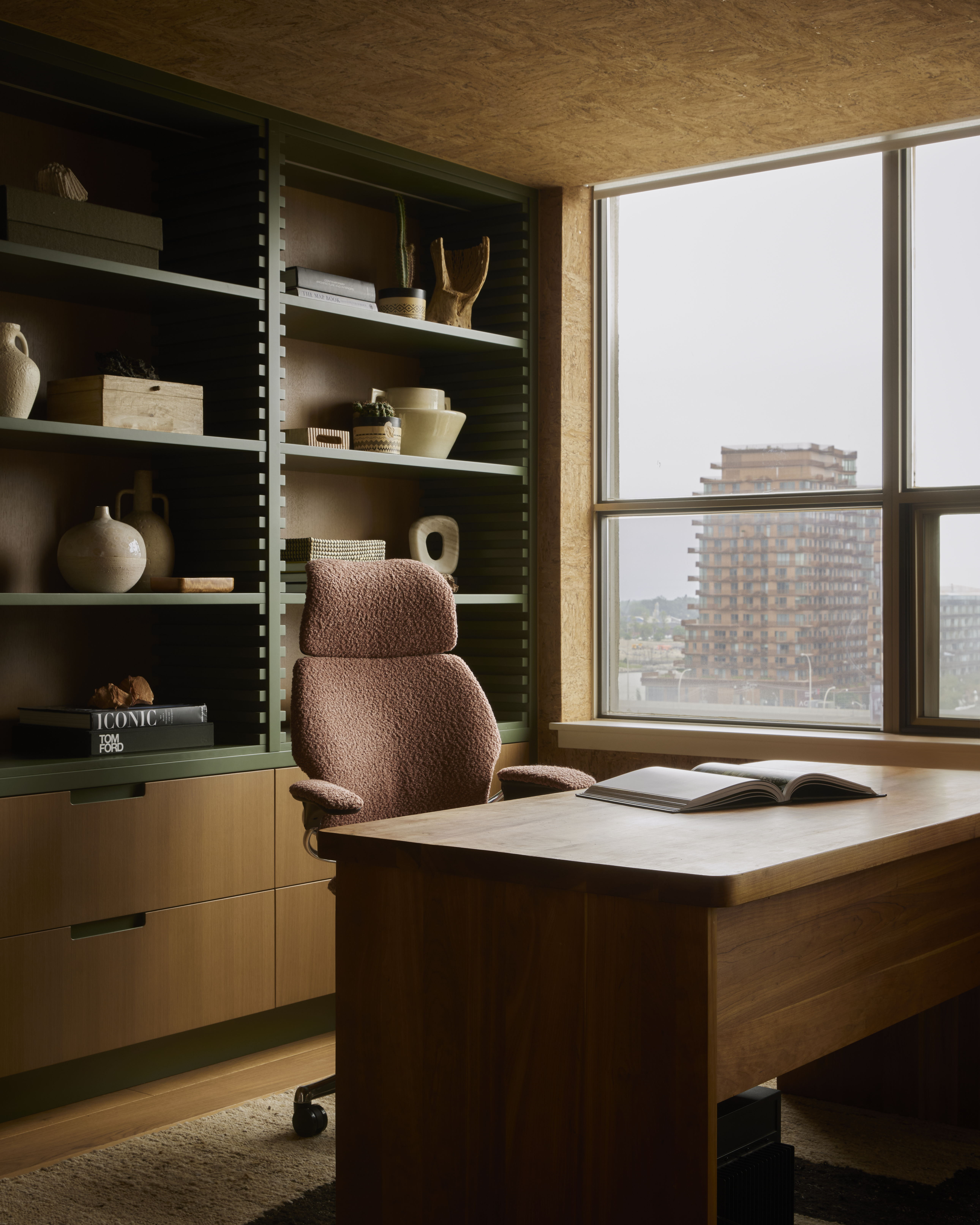 The home office combines warm walnut, cork-lined surfaces and a custom green shelving system, creating a calm, tactile workspace.