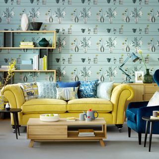Yellow sofa and blue cushions in front of patterned wallpaper