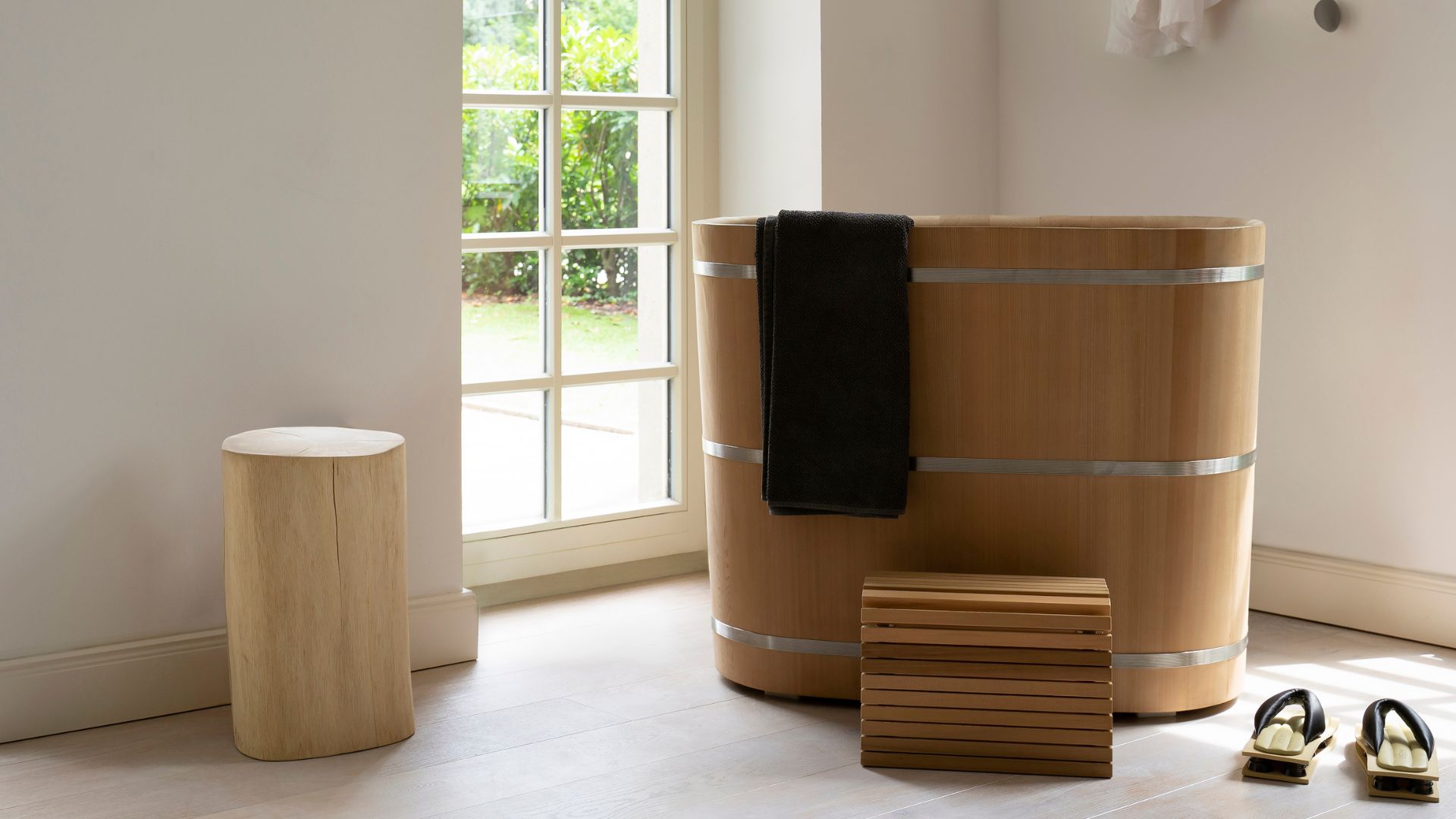 A Japanese soaking tub and wooden stool, a pair of home slippers, and a wooden plinth