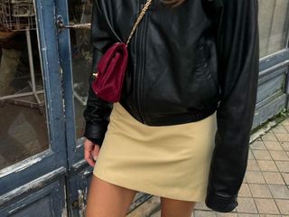 Cropped image of @annelauremais wearing a spring outfit of a yellow miniskirt, black jacket, and maroon bag