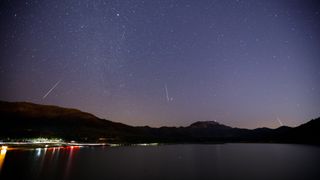 several meteor trails through a starry sky above a lake.