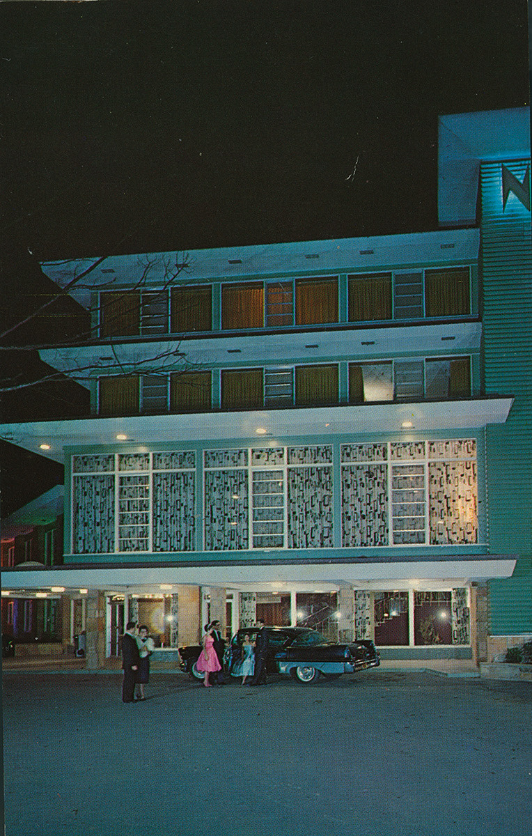 A 1950s hotel's facade is captured featuring geometric windows and motifs and a group of guests dressed for the night and stepping out of a black car.