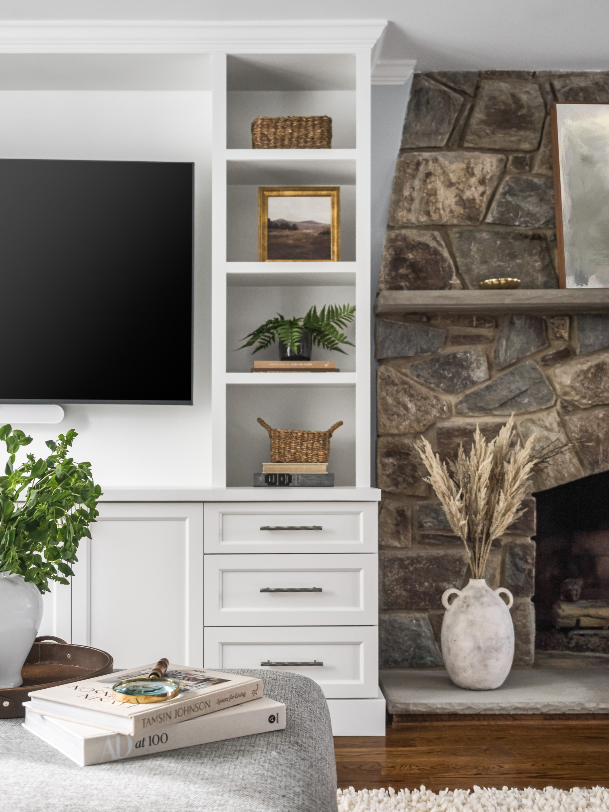 A living room with a stone fireplace and white built-in shelving with storage baskets