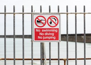A no swimming sign in front of fenced off water