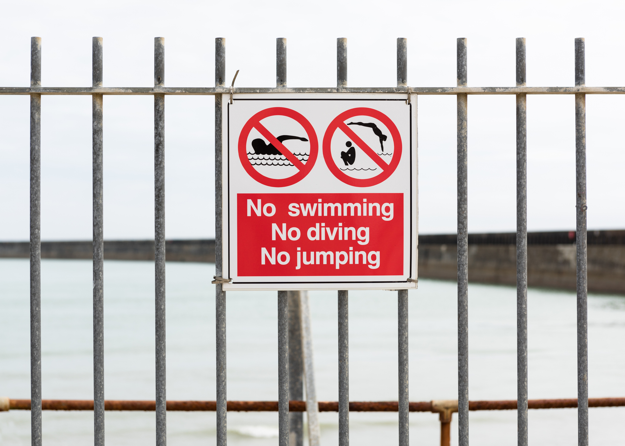 A no swimming sign in front of fenced off water
