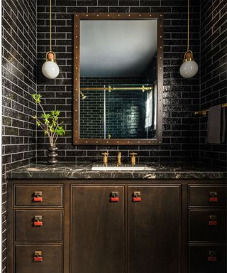 dark powder room with black tiles, dark brown vanity with black marble countertop