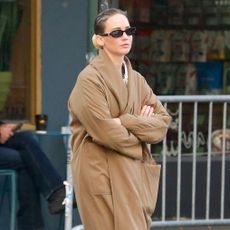 Jennifer Lawrence in NYC wearing a camel coat, large pendant necklace, white T-shirt, jeans, and Vans sneakers