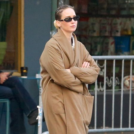 Jennifer Lawrence in NYC wearing a camel coat, large pendant necklace, white T-shirt, jeans, and Vans sneakers