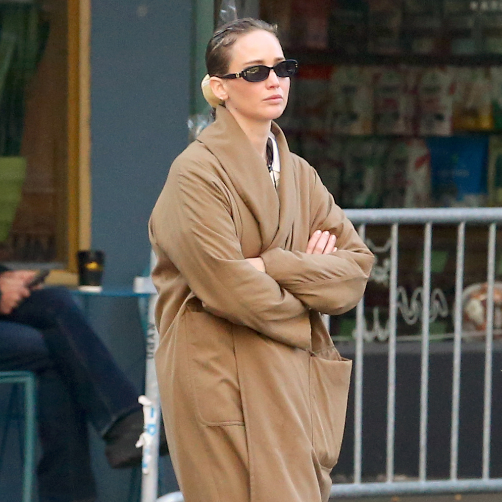 Jennifer Lawrence in NYC wearing a camel coat, large pendant necklace, white T-shirt, jeans, and Vans sneakers