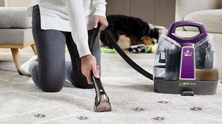 A Bissell Pet vacuum being used on a carpet marked with paw prints