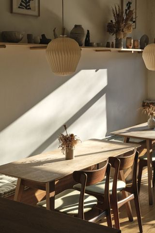 The rustic interiors of a cafe feature mid-century modern wooden furniture, scattered ceramic sculptures, rattan pendants, and plants.