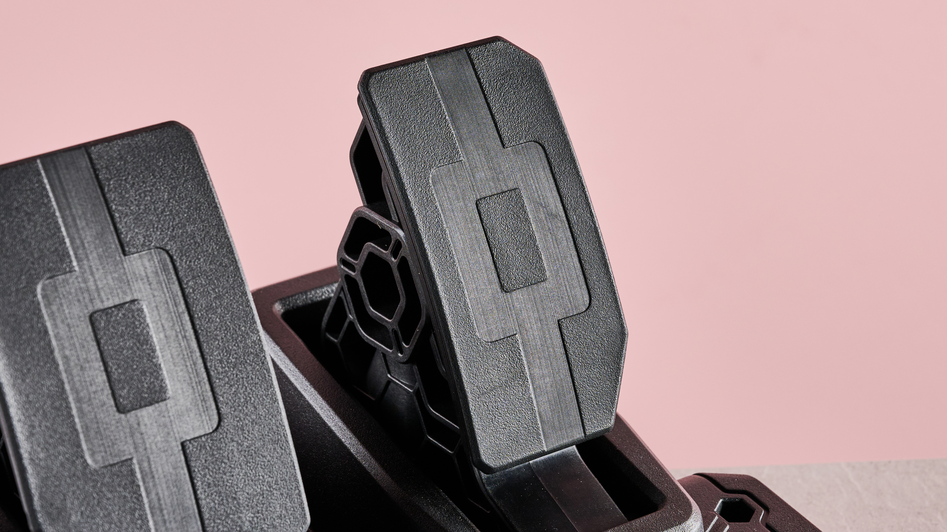 Close-up of pedals on Thrustmaster T128, on desk with pink background