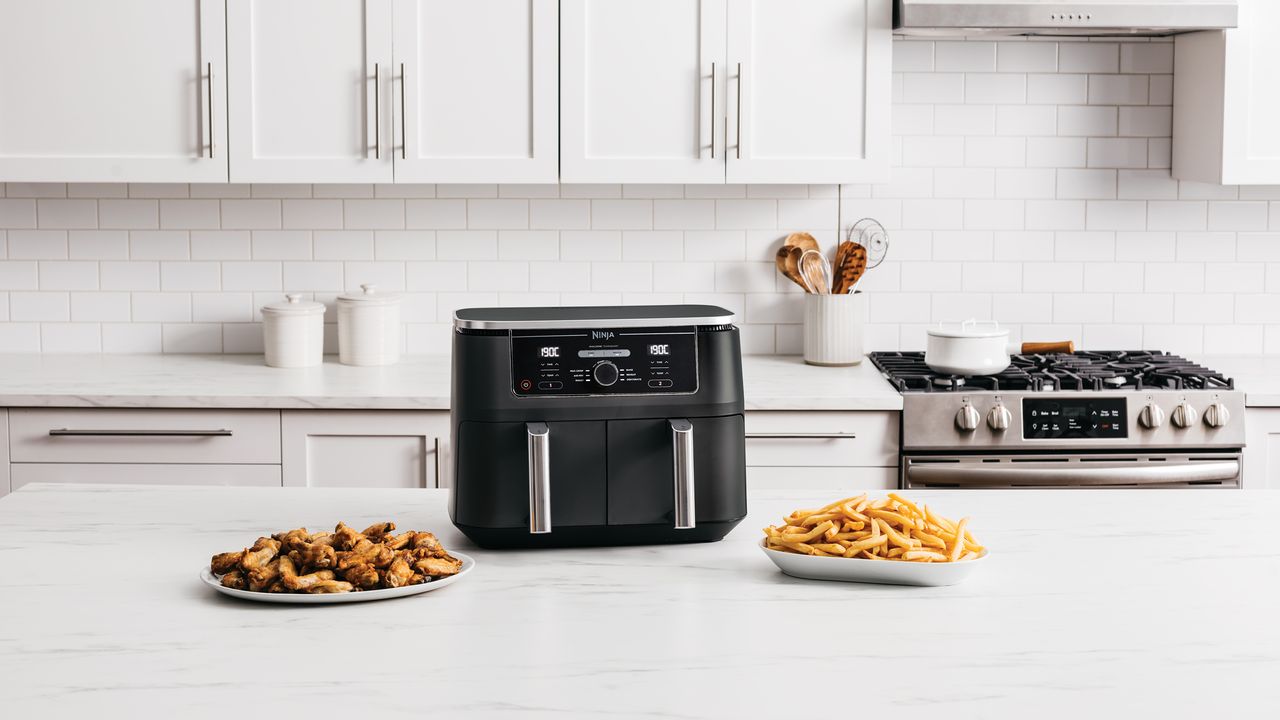 Air fryer on kitchen countertop with plates of cooked food next to it