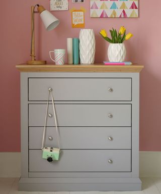 pink wall grey drawers with wooden top and lamp flower vase cup on drawers top