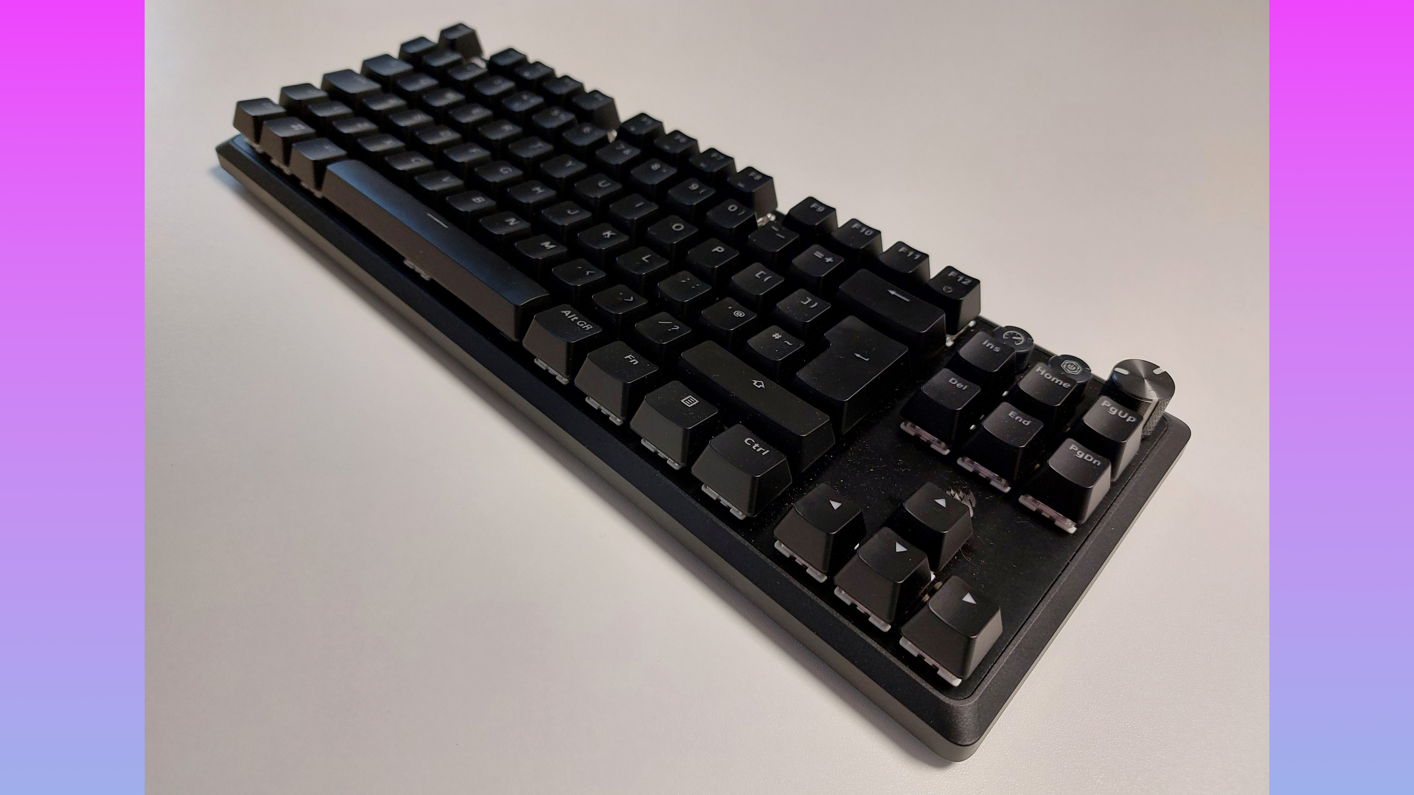 The Corsair K70 Pro TKL is seen at an angle, without the palm wrest attached. This angle offers a better look at the two media buttons and rotary dial on the board's top right hand corner.