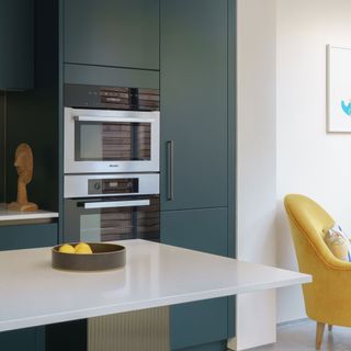 modern green kitchen with built in ovens and a yellow armchair
