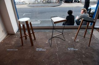 high stools on display in a store by the clear glass panel with 2 men sitting by the window outside the store