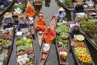 Floating market in Bangkok, Thailand, with colorful produce and Buddhist monks in orange robes.