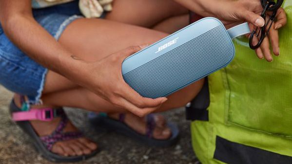 a person attaching a bose sounlink flex bluetooth speaker to a camping bag