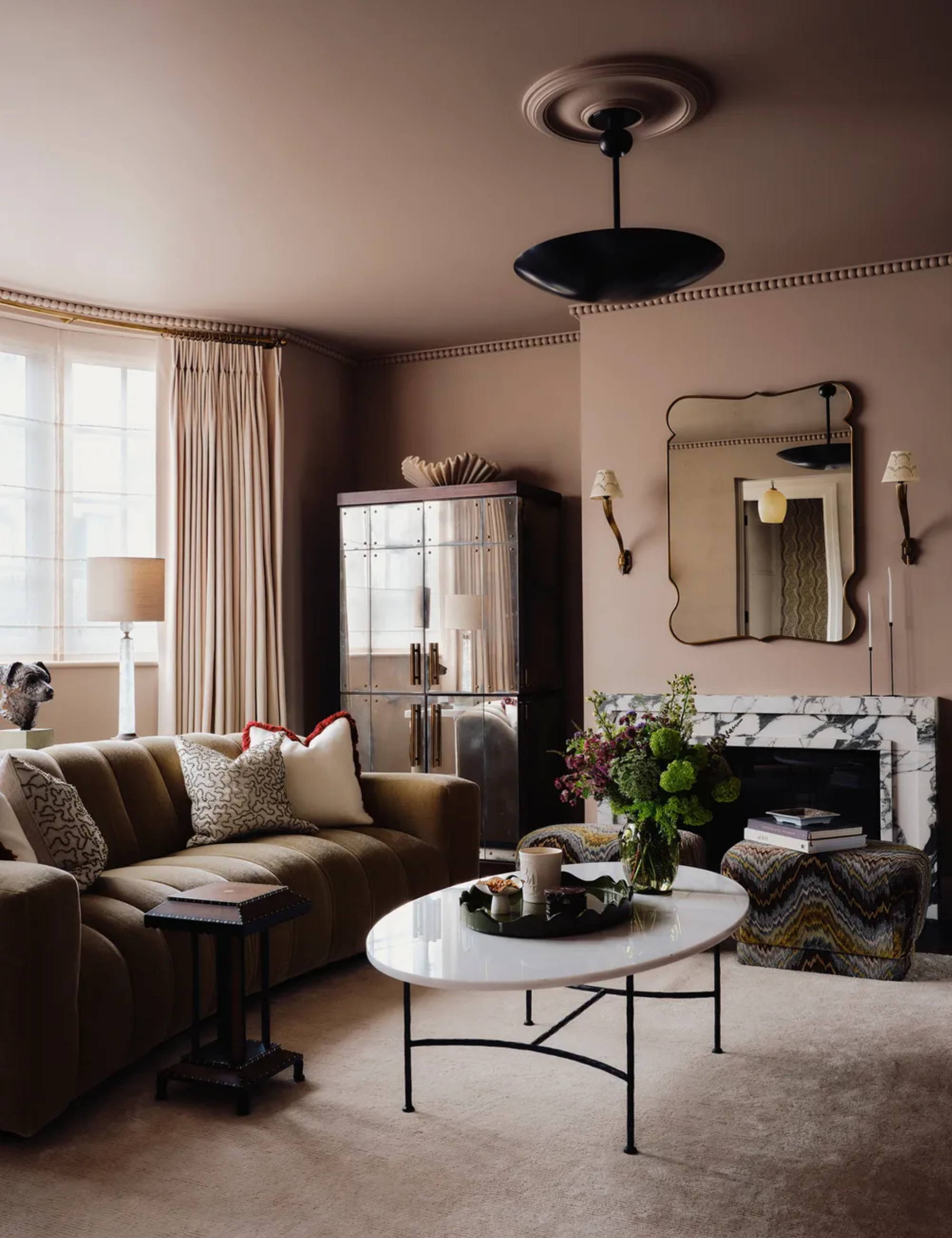 Moody neutral living room featuring softly upholstered furniture and a small, iron-legged coffee table topped with assorted objects.