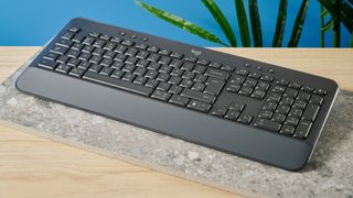 a black full sized keyboard with batteries and a palm rest on a clean beige surface with a blue backdrop