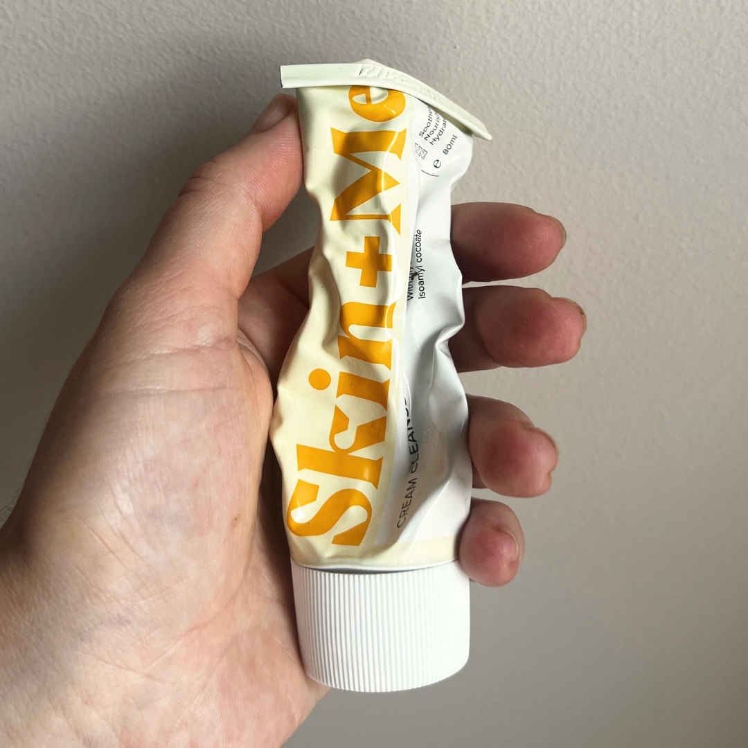 Hand holding empty tube of Skin + Me Cream Cleanser