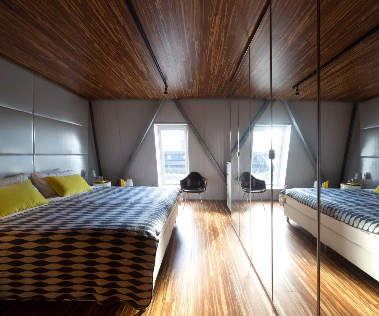 A bedroom with wooden floors and ceiling and a mirrored wall